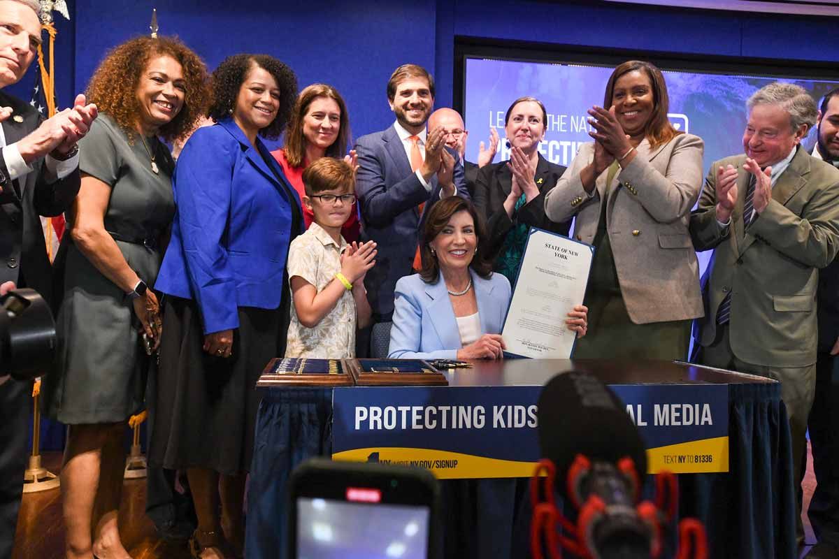 Group of people applauding behind Gov. Kathy Hochul signing a legislation